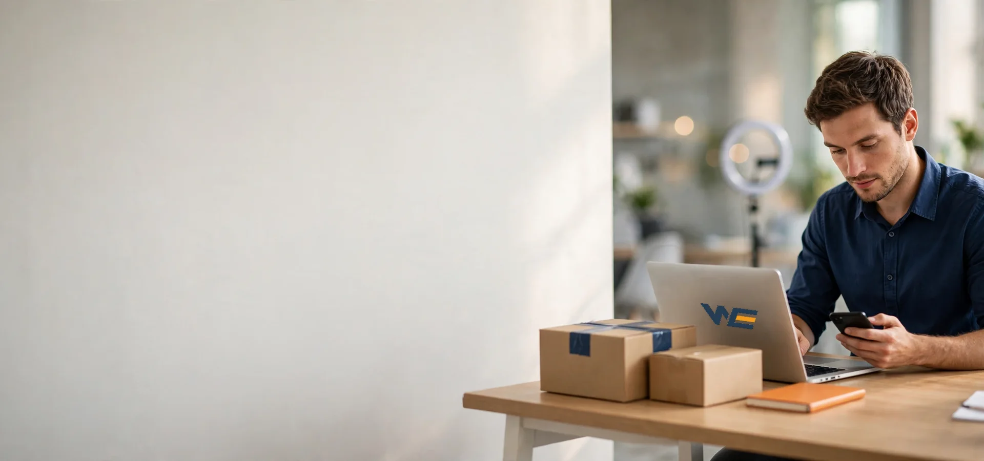Business owner checking orders on a laptop and phone, with packed product boxes on the desk